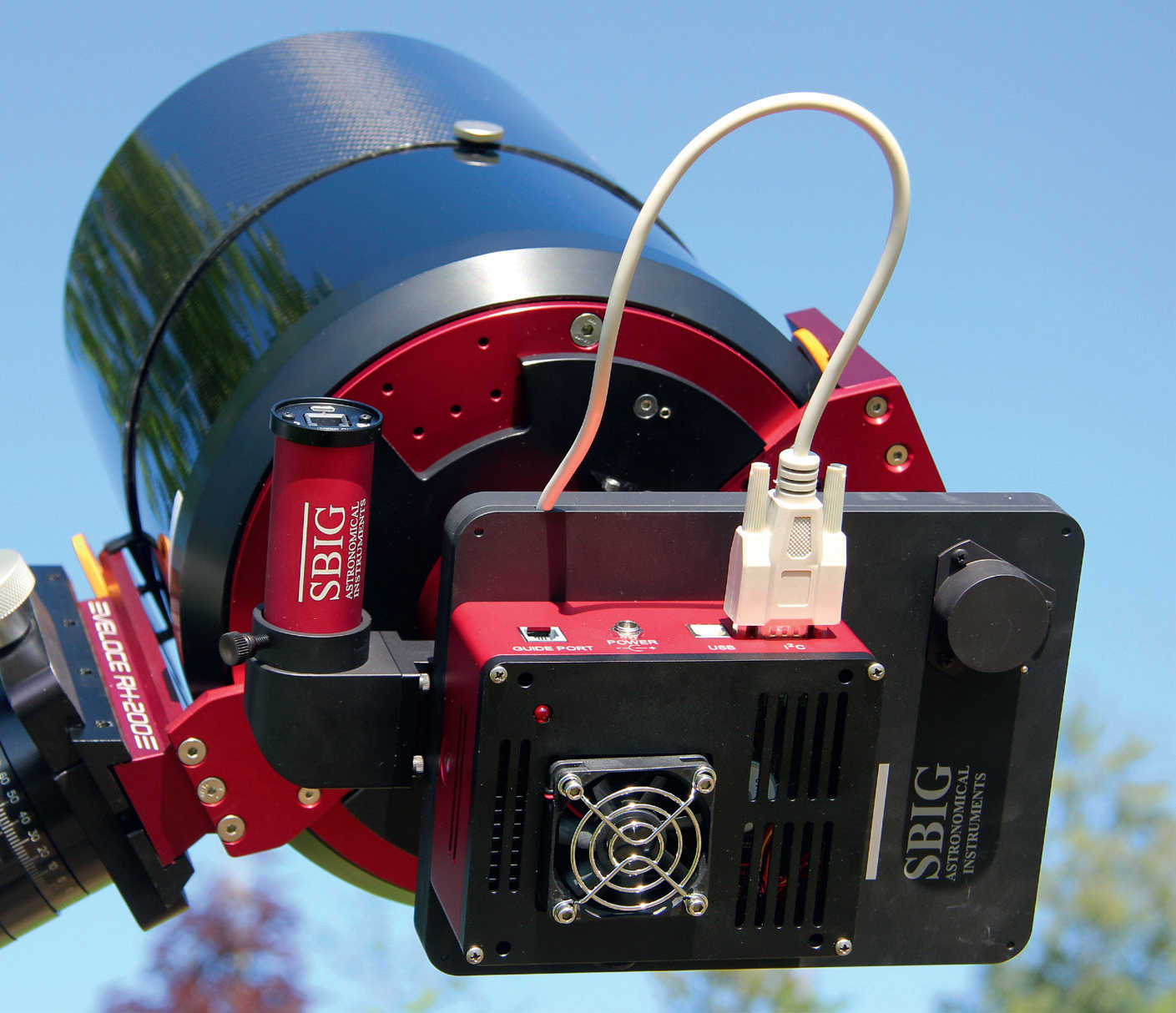A cooled CCD camera on an astrograph: the black filter wheel can be seen between the telescope and the red/black camera, and a round red autoguider can be seen next to it, which is connected to the telescope's light path using an off-axis guider. U. Dittler